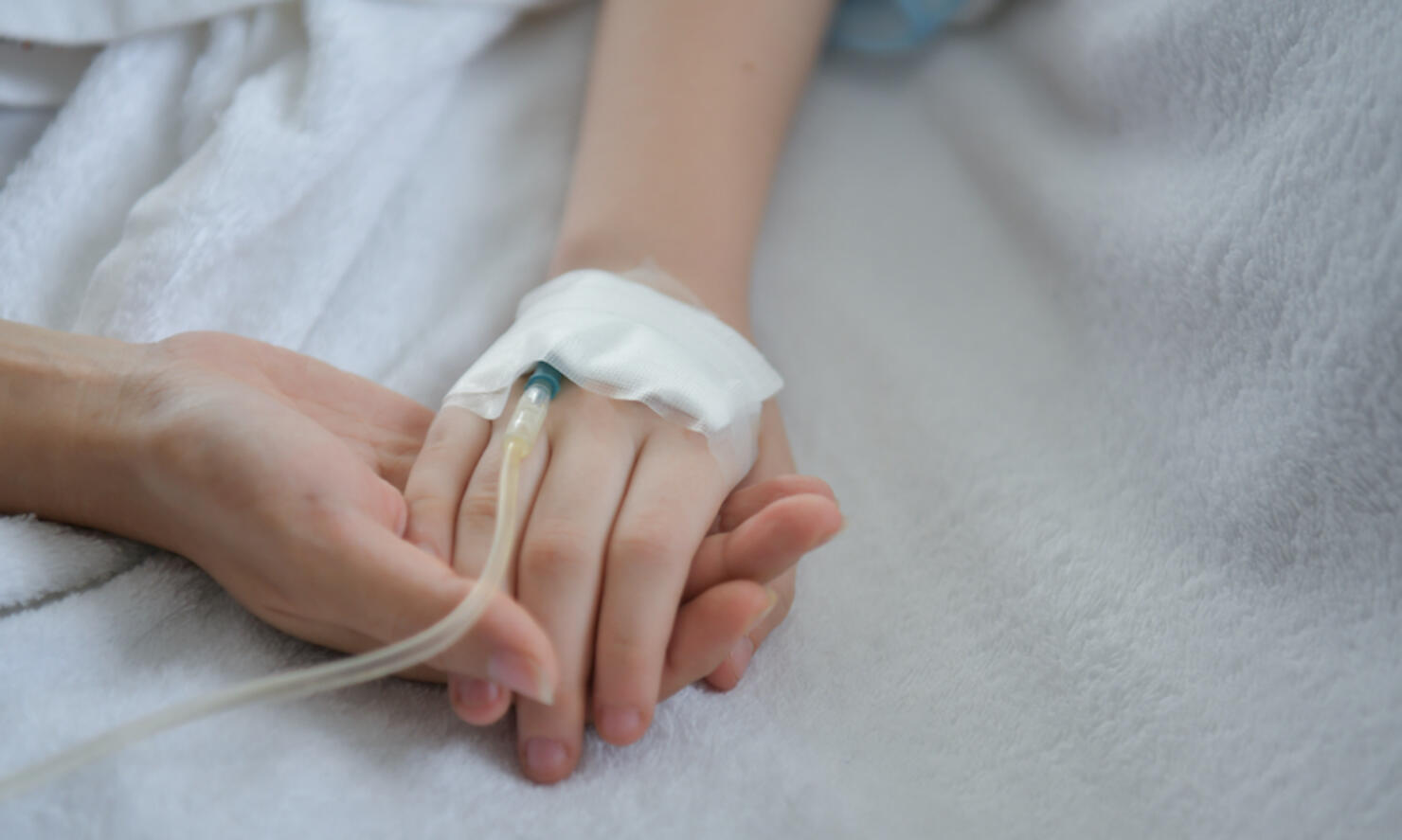 Close-Up Of Mother Holding Hands Of Medicated Child On Bed At Hospital