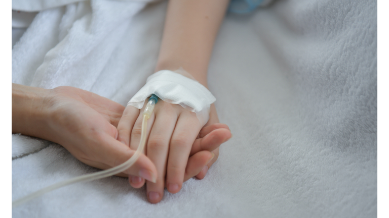 Close-Up Of Mother Holding Hands Of Medicated Child On Bed At Hospital