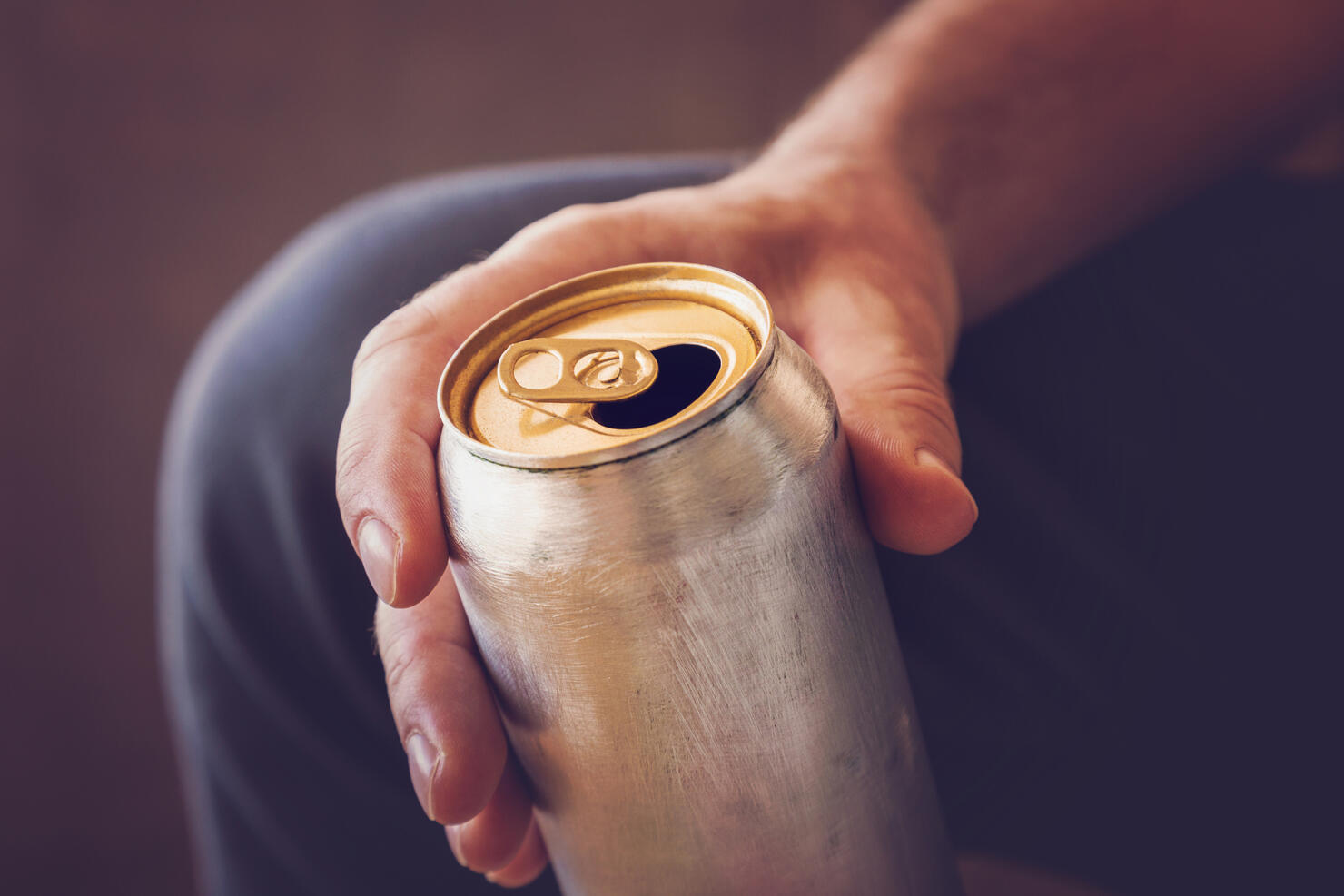 Man drinking a cold beer after work in the evening. Hand holding a aluminum can.