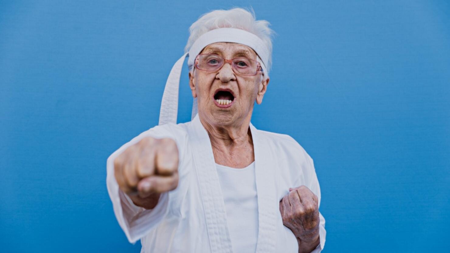 Portrait Of Senior Woman Doing Karate Against Blue Background