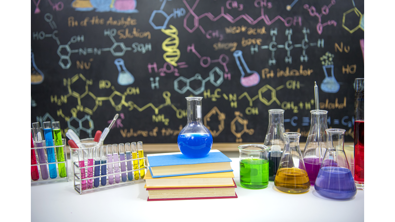 Classroom desk and drawn formula on blackboard of chemistry teaching with books and instruments.