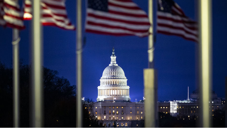 The U.S. Capitol is seen through American flags flying at half staff
