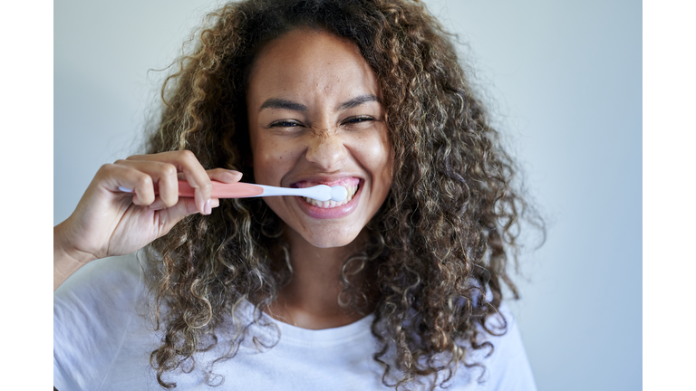 Cheerful young woman enjoying while brushing teeth against wall