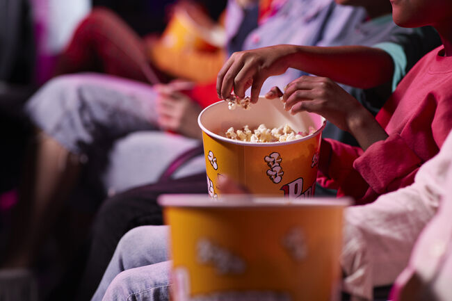Midsection of friends sharing popcorn while sitting in theater