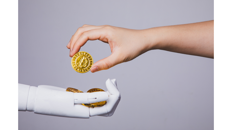 human hand taking bitcoin from robotic hand