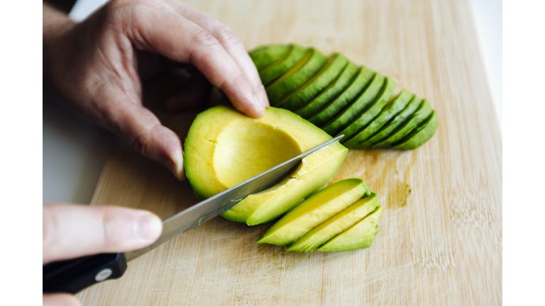 Man slicing avocado with a knife on a cutting board close up