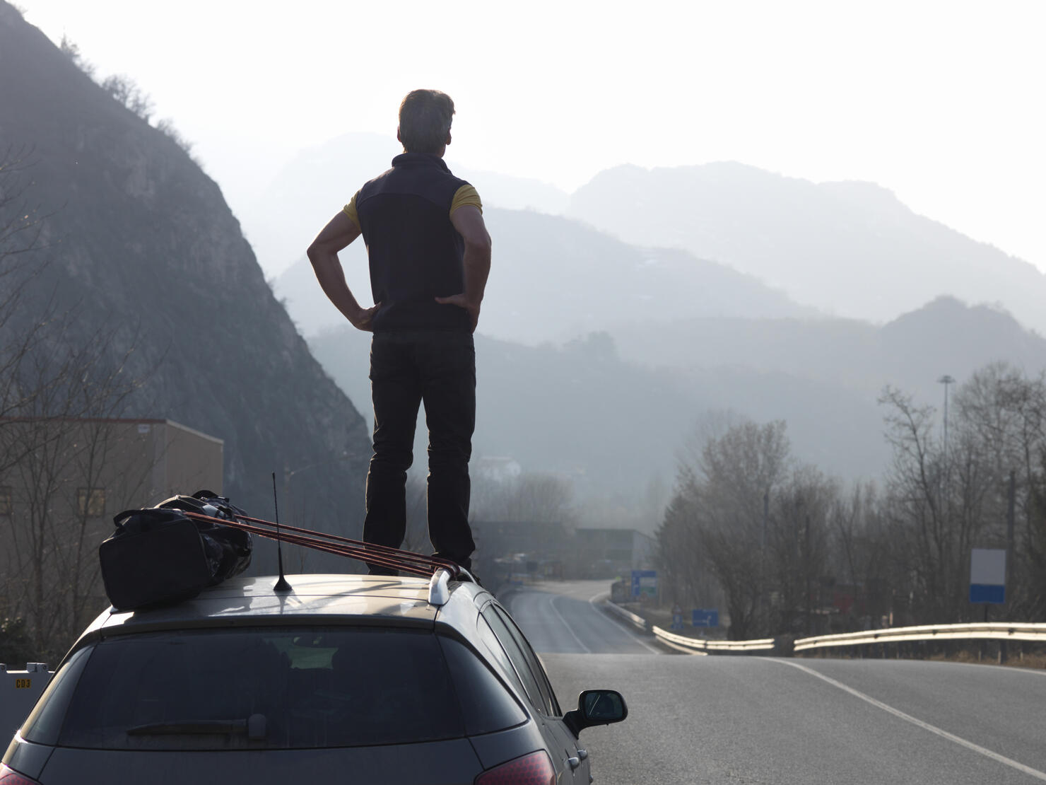 Man standing on car, looking down empty road