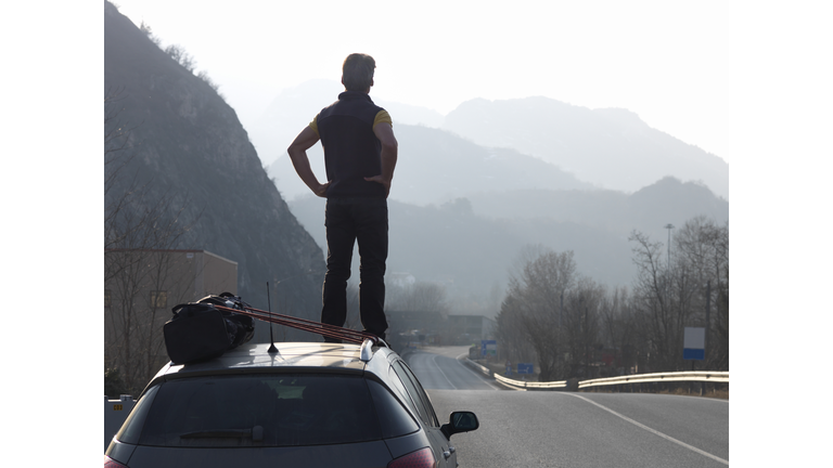 Man standing on car, looking down empty road