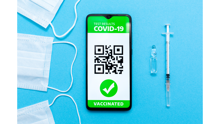 Health and medicine. Electronic Immunity passport with a COVID-19 vaccination stamp and qr-code on a smartphone screen with vaccines, syringe and protective mask on the blue background. Flat lay