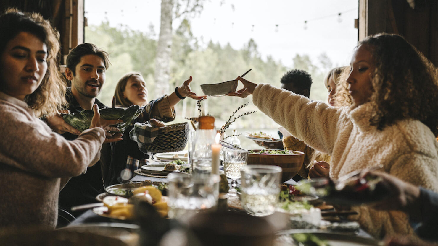 Female passing food bowl to friend over table during social event