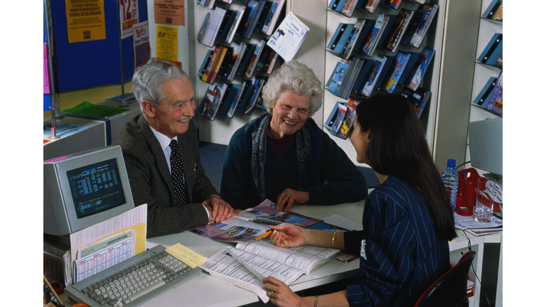 Elderly couple booking holiday, talking to female travel agent