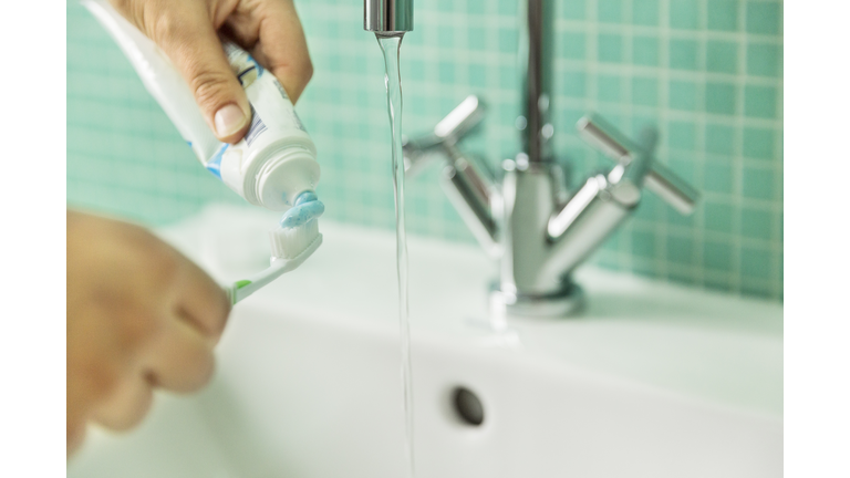 Hands putting toothpaste on toothbrush in bathroom