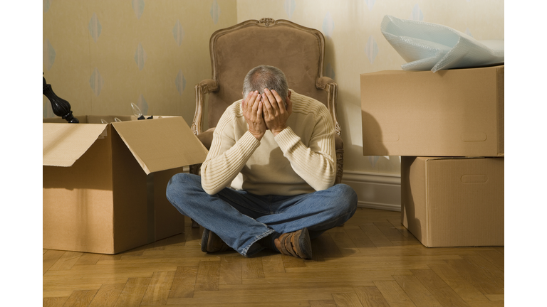 Mid adult man sitting on a hardwood floor and suffering from a headache