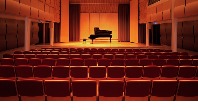 image of a piano on stage inside an empty concert hall