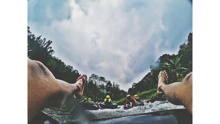 Low Section Of Man River Rafting On Inflatable Ring Against Cloudy Sky