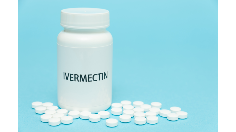 Treatments for Coronavirus (COVID-19): IVERMECTIN in white bottle packaging with scattered pills. Isolated on blue background. Horizontal shot. Copy space