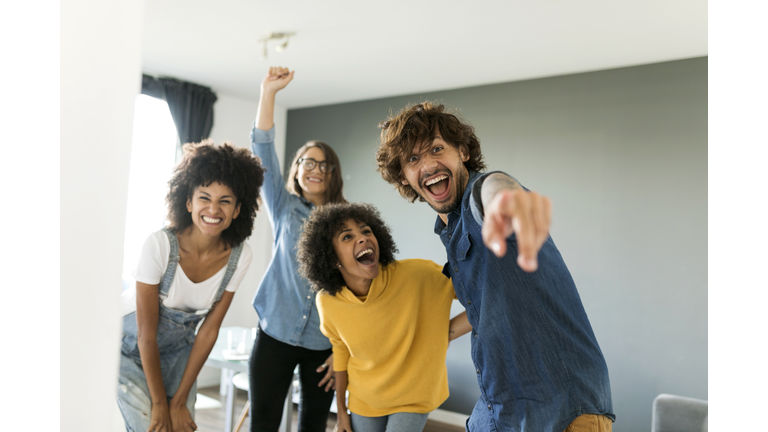 Portrait of cheerful friends at home with man pointing his finger