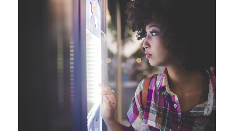 Young woman with afro hairdo using touchscreen vending machine in the city