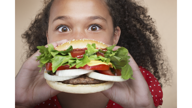 Young girl indoors eating a hamburger