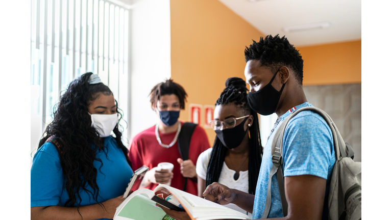 Students wearing face mask showing note pad notes to colleagues in the university / high school's corridor