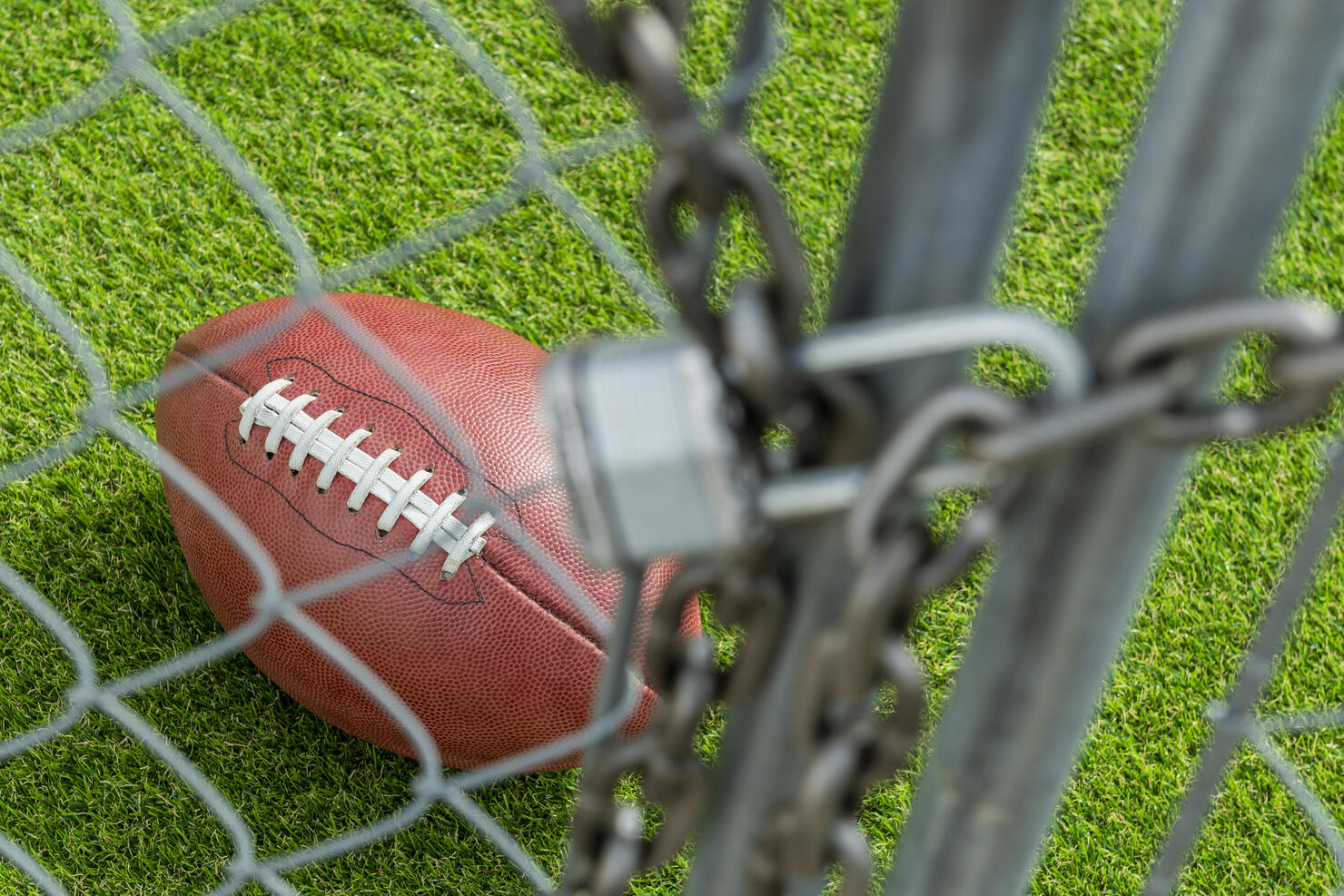 Looking through a chainlink fence gate that is locked with a padlock at American Football