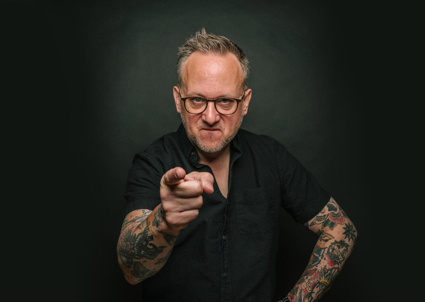 Middle-aged man with tattoos pointing at camera, angry