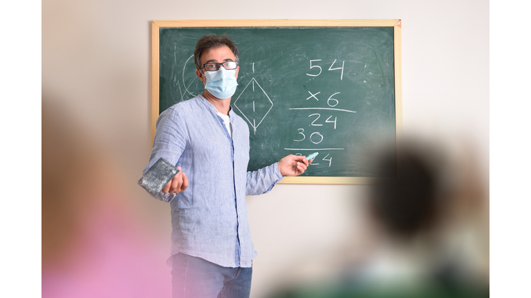 Portrait of teacher writing on blackboard in classroom