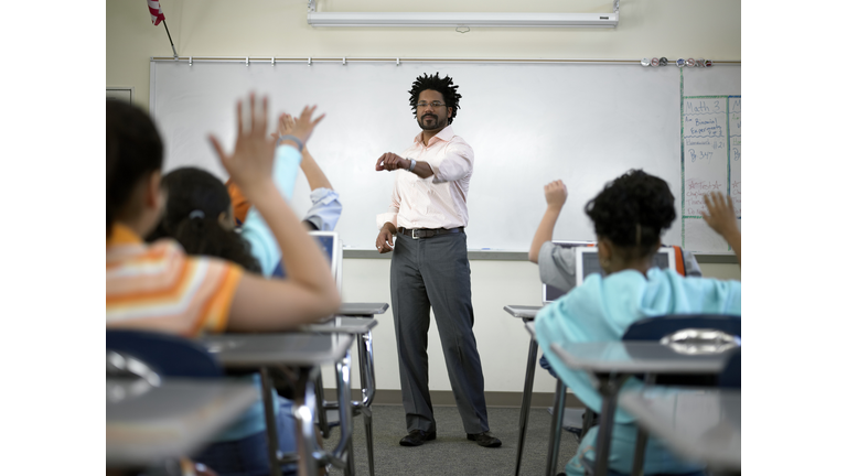 Male teacher standing before students (8-10) with hands raised