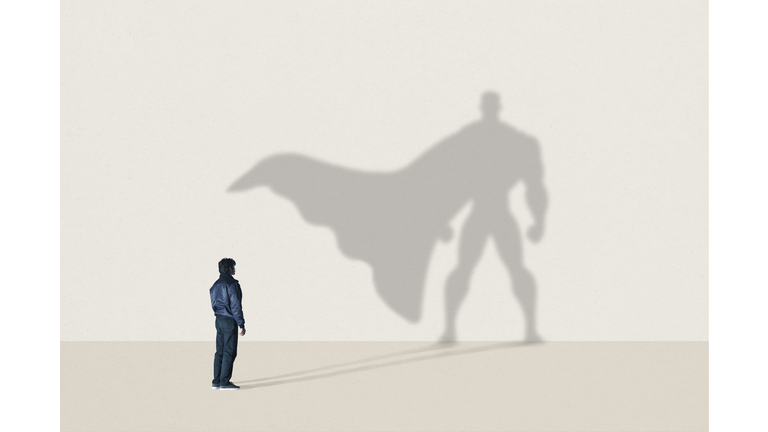 Young man standing in front of superhero shadow