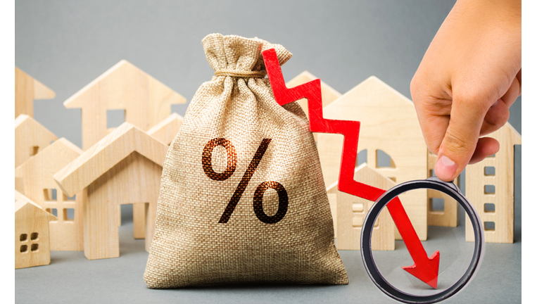 Money bag with percents, down arrow and miniature houses. The concept of low interest rates on mortgage loans or rentals. The percentage of real estate sales. Tax interest. Loan secured. Drop and fall