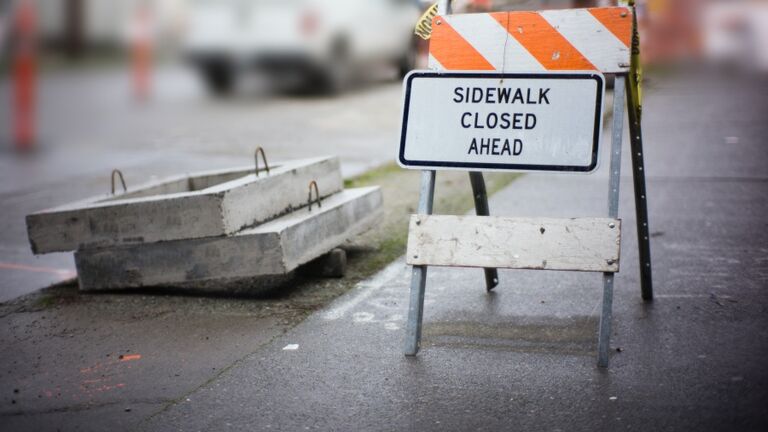 Detour sign on city sidewalk outside a construction site