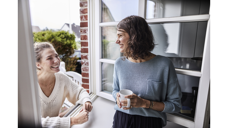 Two happy women talking through the window