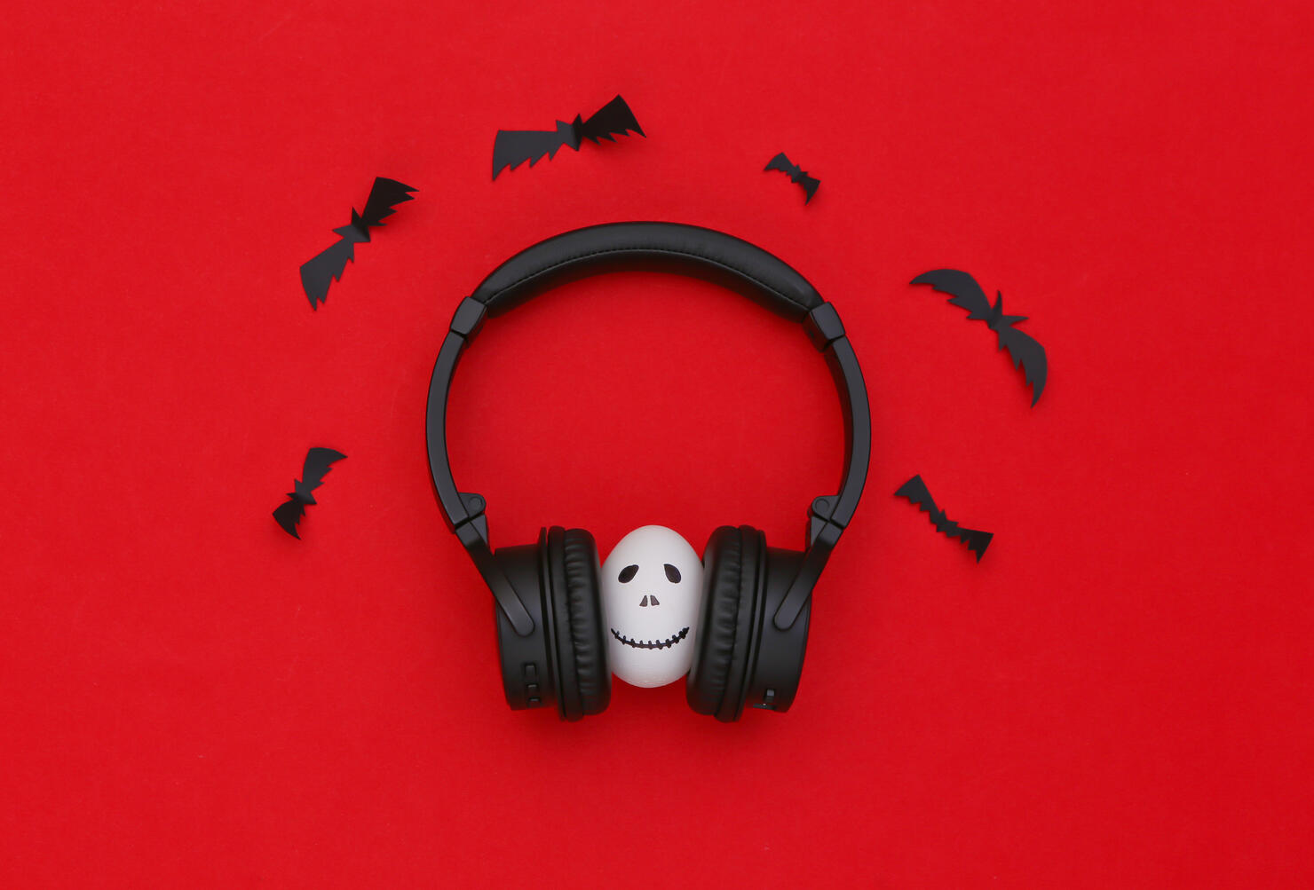 Halloween theme. Egg with hand drawn scary ghost face listen music in headphones on red background