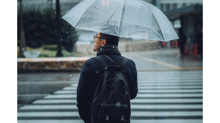 Rear view of man with umbrella walking in city in snow during Winter