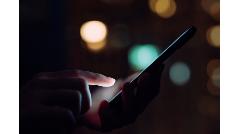 Close up of woman's hand using smartphone in the dark, against illuminated city light bokeh