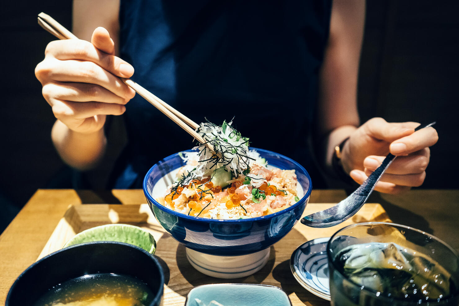 Close up of woman enjoying freshly served traditional Japanese seafood donburi with chopsticks in a restaurant