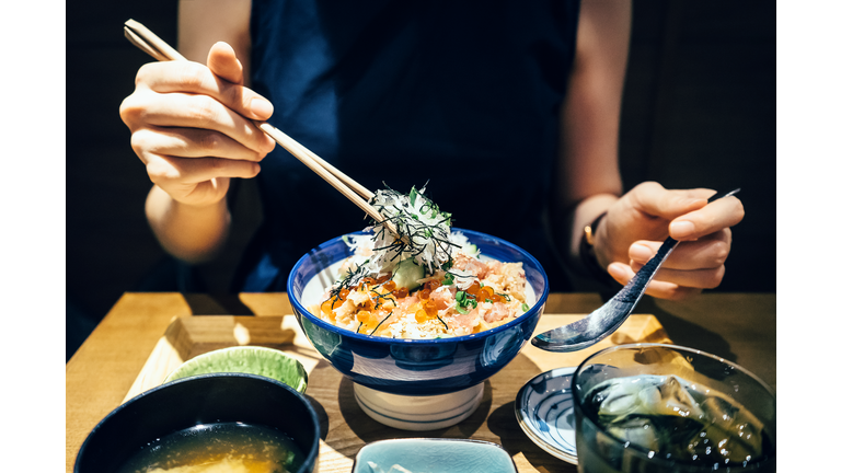 Close up of woman enjoying freshly served traditional Japanese seafood donburi with chopsticks in a restaurant