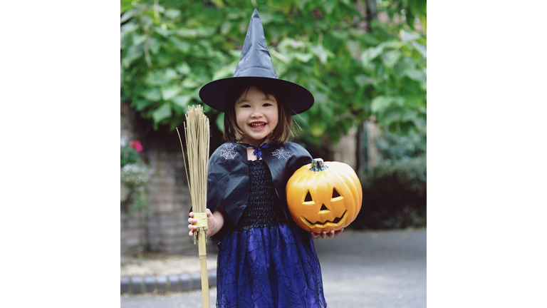 Girl (3-5) dressed as witch, holding pumpkin and broom, portrait