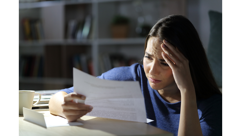 Worried girl reads bad news on letter at night at home