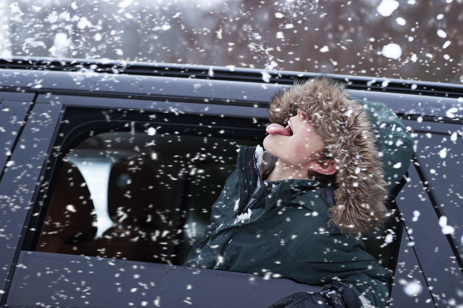 Boy tasting snow through car window during snowfall