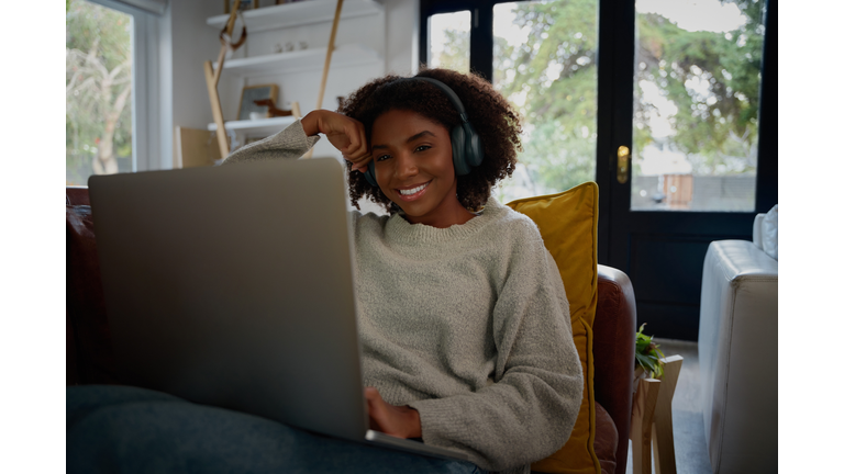 Cheerful african woman listening to audio in headphones while watching video on laptop at home