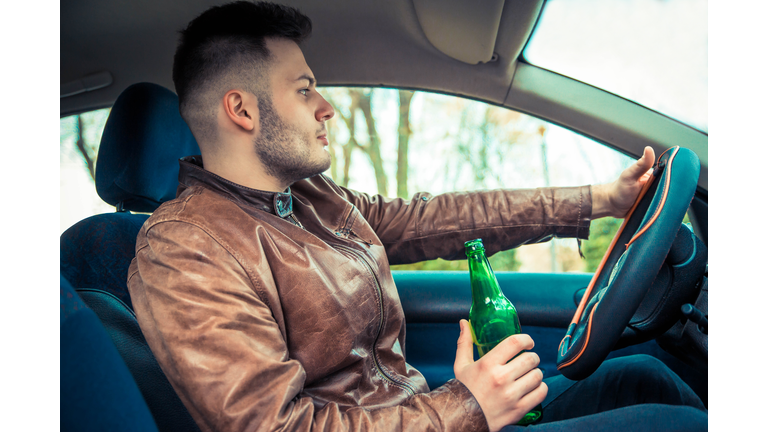 Man holding bottle of beer while driving car