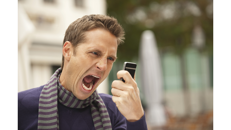 Germany, Bavaria, Munich, Man holding mobile phone, screaming, portrait