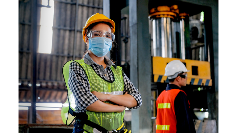 Factory woman worker or technician with hygienic mask stand with confident action with her co-worker  as background