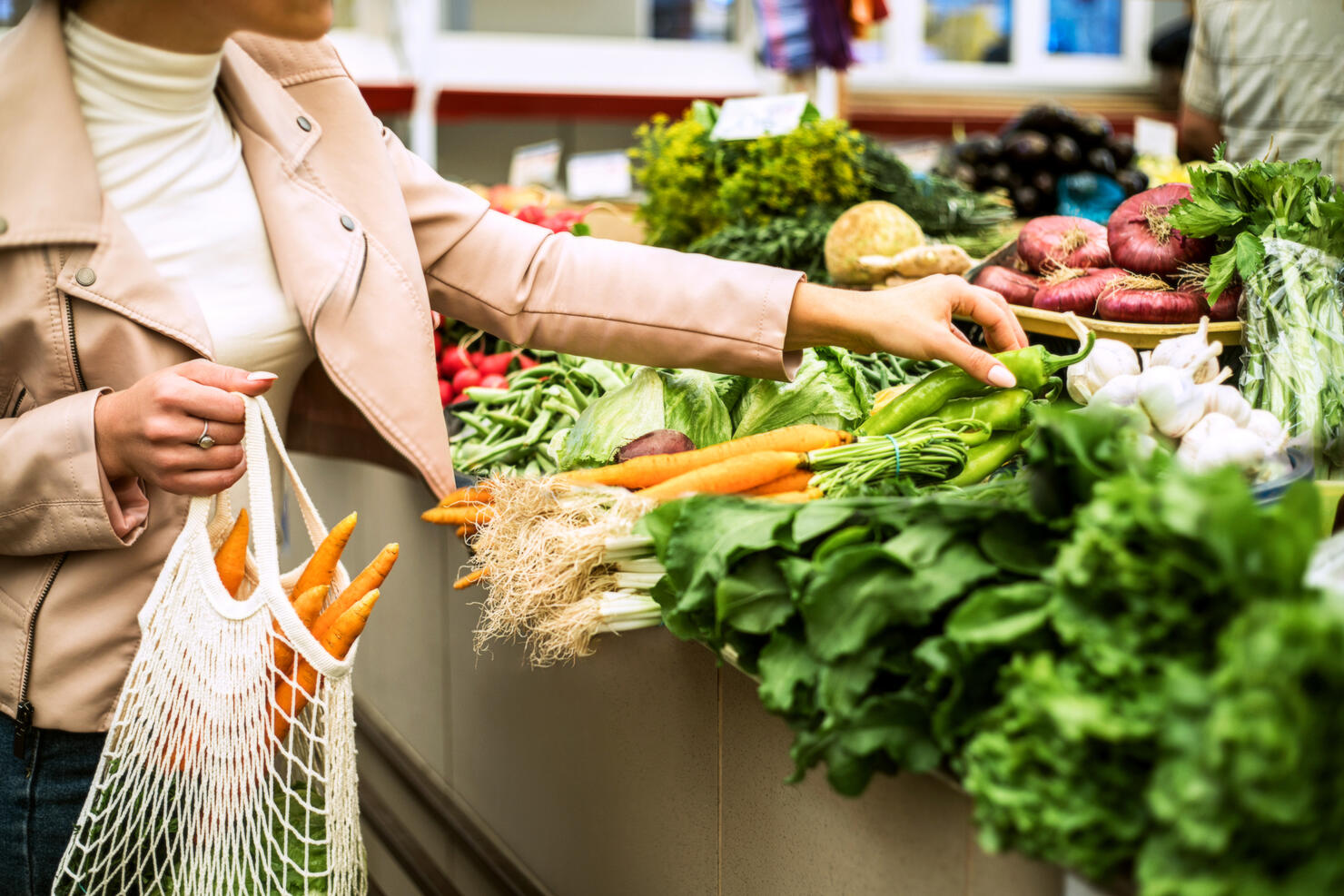 Woman choosing greenery and vegetables at farmer market and using reusable eco bag.