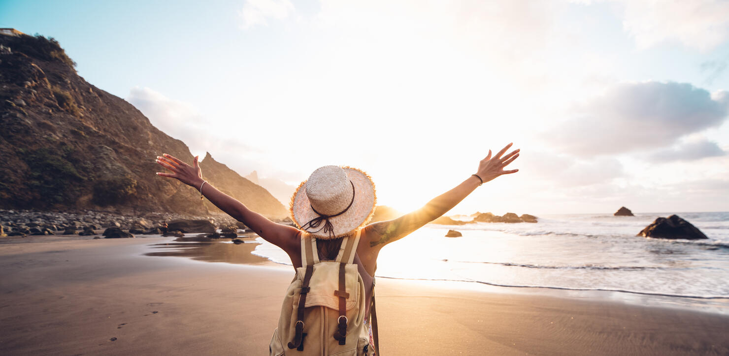 Rear View Of Man With Arms Outstretched Standing At Beach Against Sky