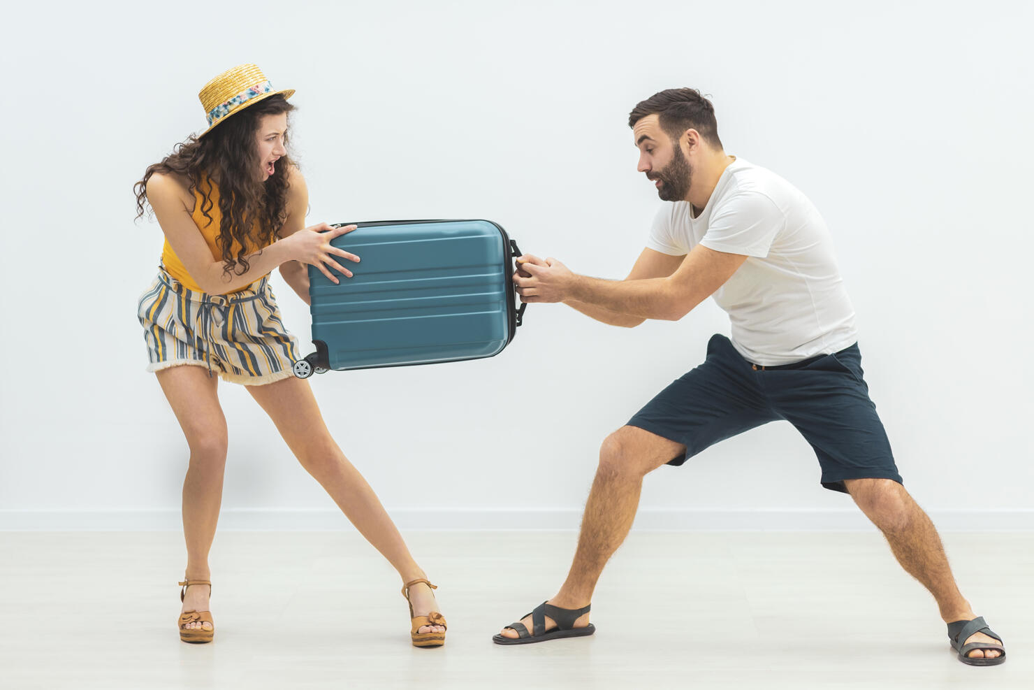 Young man and woman fighting and arguing each pulling on one end of a suitcase.