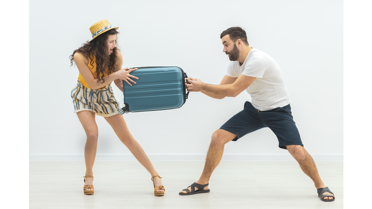 Young man and woman fighting and arguing each pulling on one end of a suitcase.
