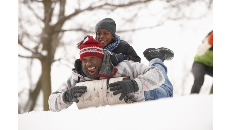 African American father and son sledding on snowy hill