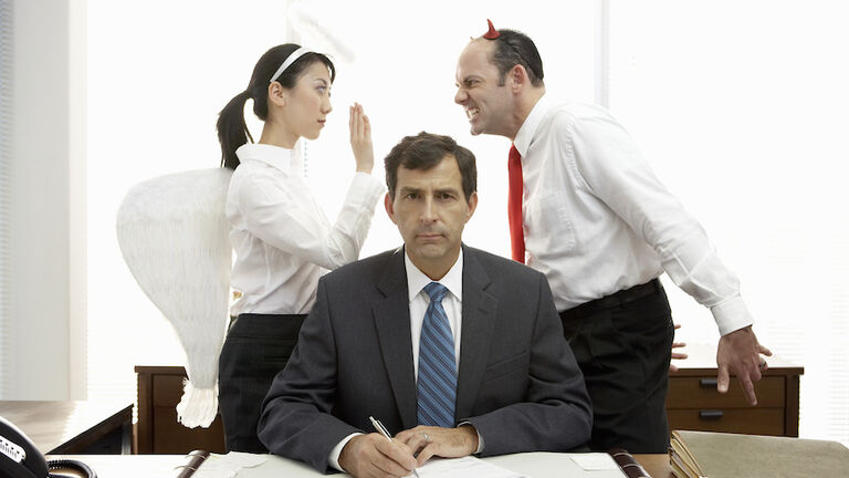 Executives with halo and devil horns standing behind businessman